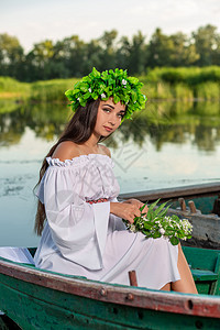 深色头发长发的女神 穿着白色古董礼服 坐在河中央的一条船上魔法花朵裙子神话海滩若虫童话魅力成人冒充图片