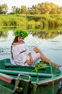 深色头发长发的女神 穿着白色古董礼服 坐在河中央的一条船上花朵魅力裙子成人魔法女孩美人鱼冒充神话若虫图片