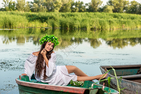 深色头发长发的女神 穿着白色古董礼服 坐在河中央的一条船上海滩若虫裙子童话女孩神话花朵魔法美人鱼冒充图片