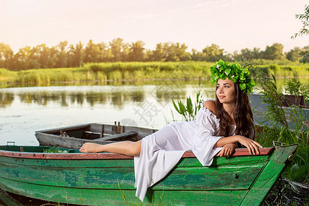 深色头发长发的女神 穿着白色古董礼服 坐在河中央的一条船上女孩童话神话海滩美人鱼若虫冒充花朵裙子魅力图片