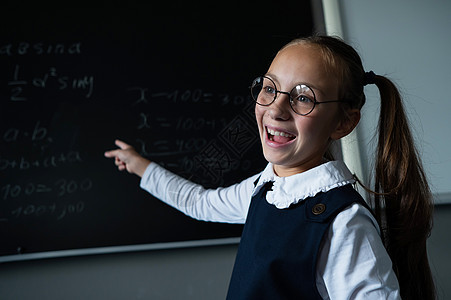 教室里戴眼镜的白人女孩的画像 女学生用粉笔在黑板上写下公式 然后看着镜头学生导师知识班级科学老师木板学校学习大学图片