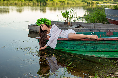深色头发长发的女神 穿着白色古董礼服 坐在河中央的一条船上魔法神话成人海滩童话花朵女孩冒充美人鱼魅力图片