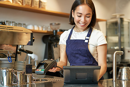 微笑的亚洲咖啡师女孩处理订单 在 POS 终端输入订单 在咖啡店柜台工作工人卡片收银机女性职员食物女士围裙服务信用图片
