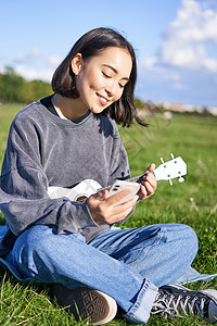 用智能手机 玩呼乐 在唱歌 户外放松时朗读和弦或歌词 放轻松 垂直拍摄笑笑的亚洲女孩成人吉他快乐歌曲弦琴乐器音乐花园音乐家爱好图片