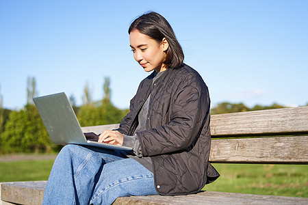 数字游牧女青年在公园使用笔记本电脑 坐在长椅上工作 在线学习的肖像学生黑发女孩微笑游民喜悦歌曲程序员幸福成人图片