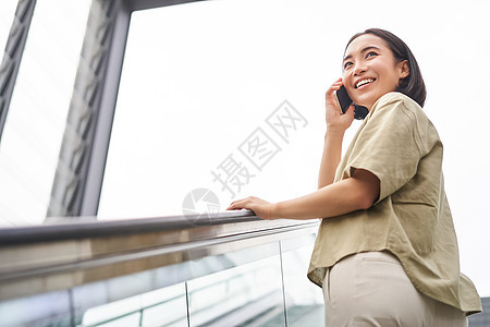 快乐的亚洲女性在扶梯上 在手机上聊天 在城里遇到某人街道城市电话细胞女孩黑发学生出租车青少年技术图片