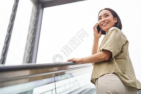 快乐的亚洲女性在扶梯上 在手机上聊天 在城里遇到某人电话技术黑发出租车互联网学生城市街道细胞青少年图片