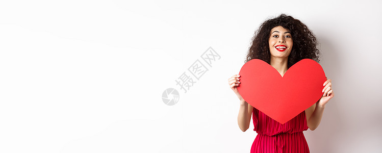 穿着衣服的浪漫女人 表现出红色的大心脏 坠入爱河 微笑快乐在相机上 白色背景卷曲情感女士伙伴展示礼物女性盒子嘴唇情人图片