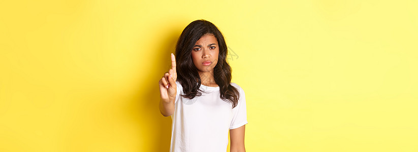 失望的非洲美国女孩说不 摇动手指来禁止或阻止某人 与人持不同意见 站在黄色背景上站立的画面多样性发型黑发工作广告潮人情感手势女士图片