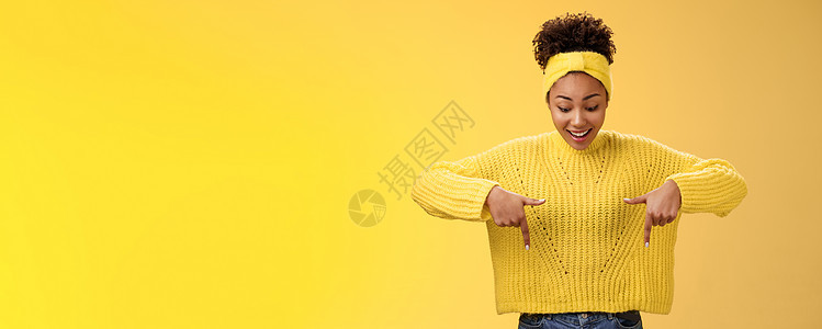 身穿毛衣头带 热情微笑 着迷的非洲裔美国女性印象深刻 她指着食指 喘着粗气 惊讶地着迷 酷酷的惊心动魄的宣传片 站立的黄色背景青图片