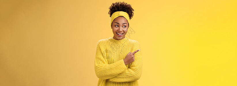 有趣的年轻可爱的千禧一代非洲女性偷看傻指左笑广泛展示好奇有趣的地方挂我们的朋友推销产品指示广告 黄色背景员工大学爆炸女朋友毛衣手图片
