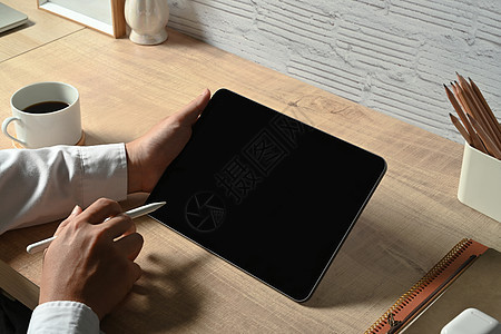 人手握着tylus笔 在网上用木制桌上的数字平板电脑工作图片