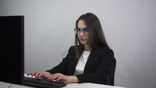 女商务人士在办公室的电脑上工作 一个穿西装戴眼镜的年轻女人 在键盘上仔细打字图片