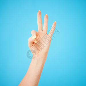 演播室拍到一个不知名的女人 在蓝色背景下举起三根手指的镜头 - 是的 我图片