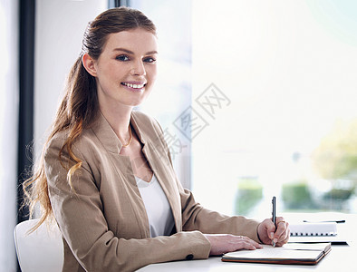 保持有条不紊是前行的关键 一个年轻女商务人士在办公室工作时写笔记的肖像图片