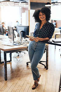 她让整个办公室充满活力 一位开朗的年轻女设计师站在她的办公室里拿着数字平板电脑的全长肖像图片