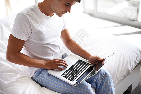 一位英俊的年轻人在床边用笔记本电脑冲浪 在床边图片