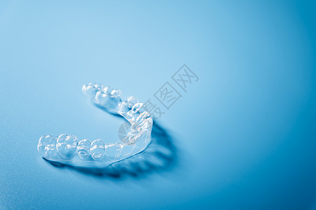 在蓝色背景和复制空间上特写看不见的连接器 塑料牙套将牙科保留员固定在牙齿上以整齐保留者矫正支撑对准器治疗技术卫生固定器保健口服图片