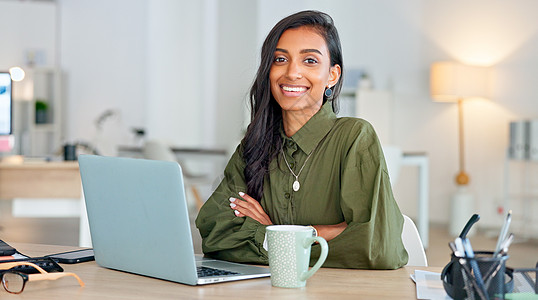 骄傲 快乐和自信的女商务人士在笔记本电脑上打字 然后转身看着她办公室的摄像头 一位年轻女企业家的肖像 她在工作场所微笑着写一个项图片