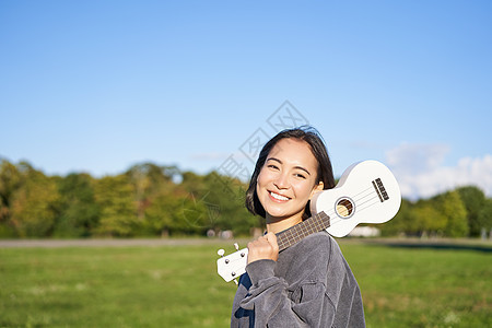 年轻的时装女孩 旅行者 抱着她的乌合乐 在公园户外玩耍和微笑吉他弦琴音乐家女性黑发快乐乐器喜悦幸福歌曲图片