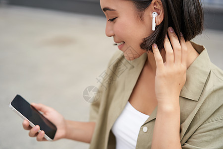 特写亚洲女孩的肖像 看着手机屏幕 戴着耳机听音乐 戴耳机的女人走在街上青少年出租车技术互联网街道城市女性音乐快乐细胞图片