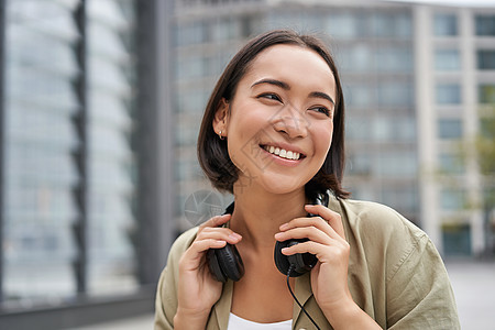 带着耳机 在市中心装扮 听音乐的笑笑的亚洲女孩的肖像城市微笑街道青年女士音乐互联网电话青少年快乐图片