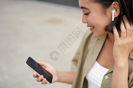 特写亚洲女孩的肖像 看着手机屏幕 戴着耳机听音乐 戴耳机的女人走在街上青少年城市女性快乐出租车黑发互联网街道音乐电话图片