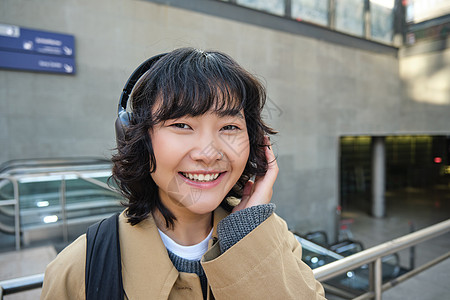 在耳机里紧贴着微笑的黑发女孩 听音乐 绕城市旅行 往返上班 站在街上技术游客咖啡学生旅游音乐互联网快乐手机城市图片