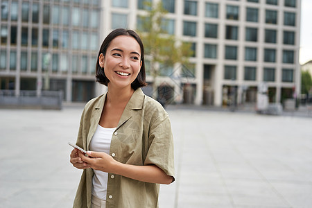 站在街上 市广场和手持手机的亚洲妇女肖像 有智能手机的女孩在户外行走学生出租车细胞互联网电话技术青少年城市街道黑发图片