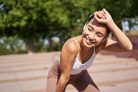 亚洲女性休息 跑步后喘息 喘息 慢跑者站着擦额头汗水 高兴地微笑女孩公园训练赛跑者瑜伽太阳运动装快乐日落运动图片