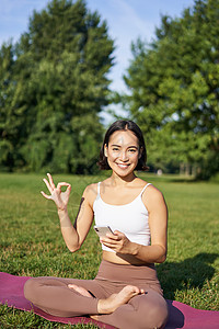 垂直拍摄的亚洲女性照片显示好标牌 建议在线瑜伽训练 冥想应用 在公园新鲜空气中做练习图片