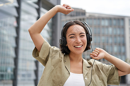 女孩在街上跳舞 戴耳机 听音乐 并感到愉快地在城市中行走手机女性技术快乐电话闲暇音乐黑发女士青少年图片