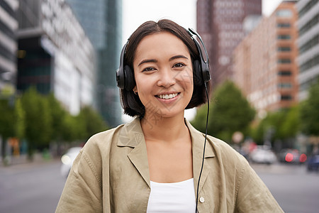 坐在市中心街上 看着快乐 听音乐的景象 在耳机中模仿着微笑的亚洲女人的肖像黑发青少年青年唱歌音乐喜悦商业技术手机街道图片