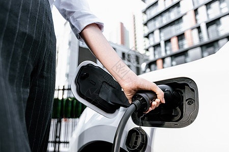 聚焦EV充电器插件 模糊的进步女性 在背景中充电EV汽车生态女士车站车辆收费杂交种商务活力民众停车场图片