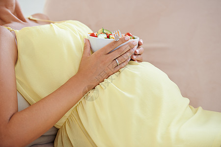 怀孕期间的健康掌握在您的手中 一名孕妇在沙发上放松 一边吃着新鲜的沙拉图片