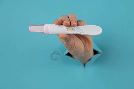 一只用蓝纸板背景的洞露出阴性怀孕测试的手 笑声女性孩子药品生育力母亲妇科症状激素药物母性图片