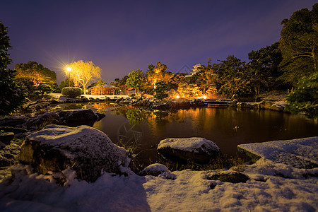 在日本花园的小池塘上下雪 寒冬夜晚有灯光图片