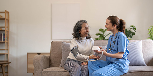 快乐的老年妇女在疗养院由护理人员测量血压 快乐的护士在客厅测量一位老年妇女的血压检查考试成人测试药品医院访问帮助脉冲男人图片