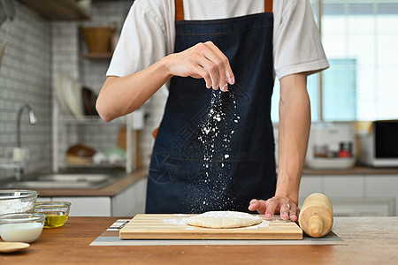 男人穿着围裙 面粉在新鲜面团上洒满面粉 在厨房桌上准备自制的糕点图片