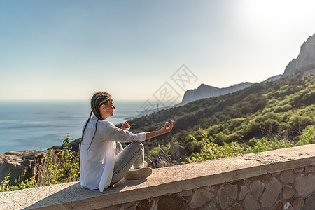 一个女人在山的悬崖顶上做瑜伽的轮廓 女人在瑜伽体式 Padmasana 中冥想图片