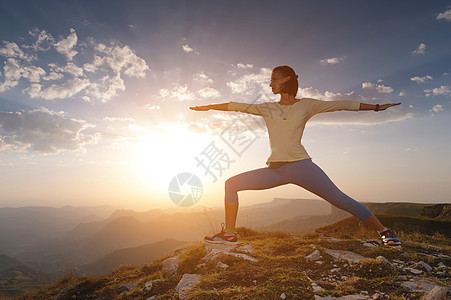 参加武术瑜伽的年轻女青年 在美丽的乌云天空下 站在山岩上图片