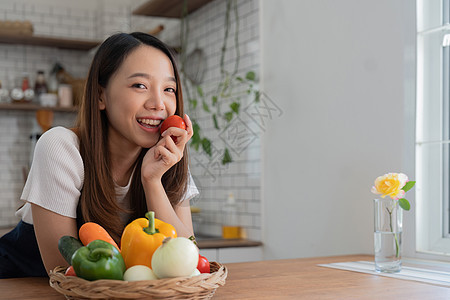 亚洲年轻女子的画像看着相机 漂亮的美女在舒适的厨房里穿着围裙 桌上摆着新鲜有机蔬菜 烹制健康蔬菜沙拉 健康食品积极生活饮食女士微图片