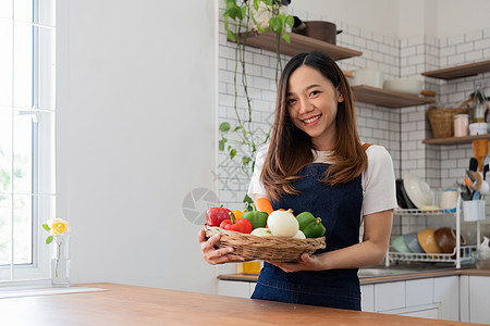 亚洲年轻女子的画像看着相机 漂亮的美女在舒适的厨房里穿着围裙 桌上摆着新鲜有机蔬菜 烹制健康蔬菜沙拉 健康食品积极生活微笑女士饮图片