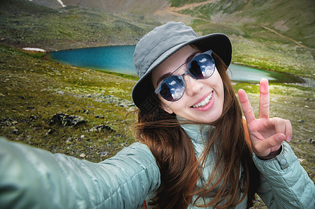 年轻快乐 笑笑的观光女游客长着棕褐发和灰色斑马带自拍与智能手机制造和平标志 在岩石山顶上手牵手图片