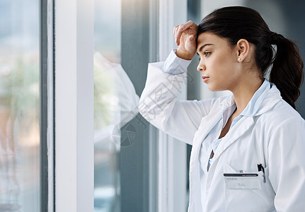 医生职业倦怠的问题越来越普遍 一位年轻的女医生站在医院的窗户前 看起来很紧张图片