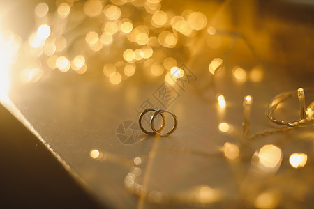 模糊散景发光的金色背景上的结婚戒指 带纹理的闪光背景上的爱情和浪漫的象征 带有复制空间供您问候或祝贺婚礼展示辉光礼物订婚配饰奢华图片