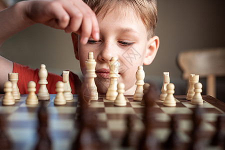年轻的白人孩子在大棋盘上下棋 小学生面前桌上的棋盘思考下一步数字主教乐趣国王典当运动象棋专注玩家女王图片
