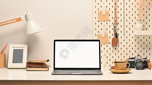 舒适工作场所 带空白屏幕的膝上型笔记本电脑 图片框 照相机和白桌上的灯图片