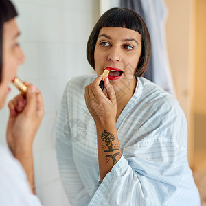 早上在浴室镜子里涂红唇膏的年轻女子 她用红色口红擦过她的浴袍后部图片