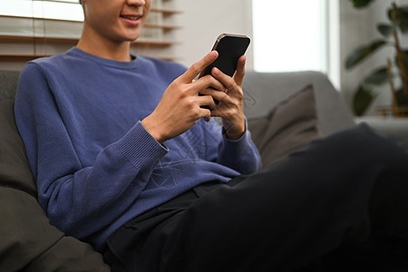 男人打短信 坐在家沙发上用手机聊天时在网上聊天的裁剪镜头图片